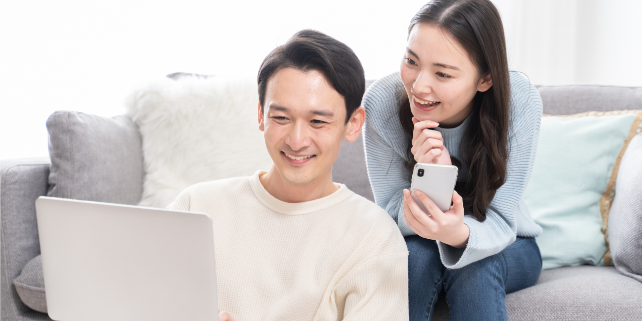 ソファでパソコンを見ながら笑い合う夫婦